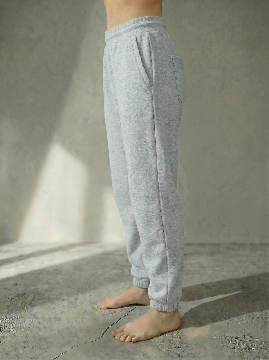 Side view of the Deryn Jogger women’s luxury jogger pants by BOU Clothing in grey, shown on a model standing barefoot against a stone gray backdrop.