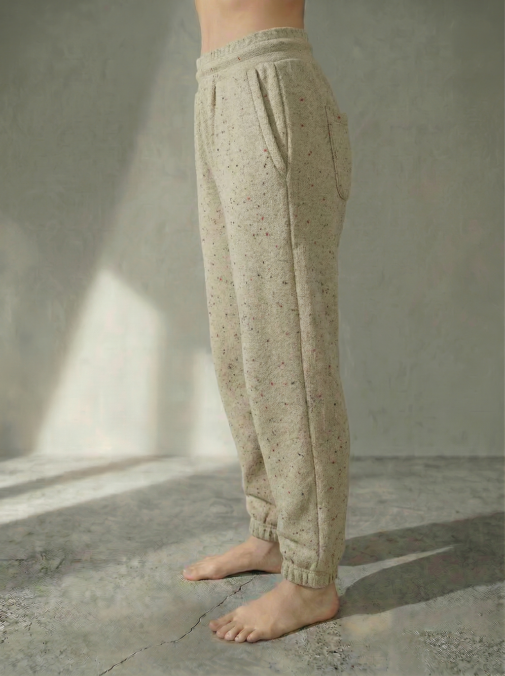 Side view of the Deryn women’s luxury jogger pants beige with red fleck colour, by BOU Clothing shown on a model standing barefoot against a stone grey  backdrop.