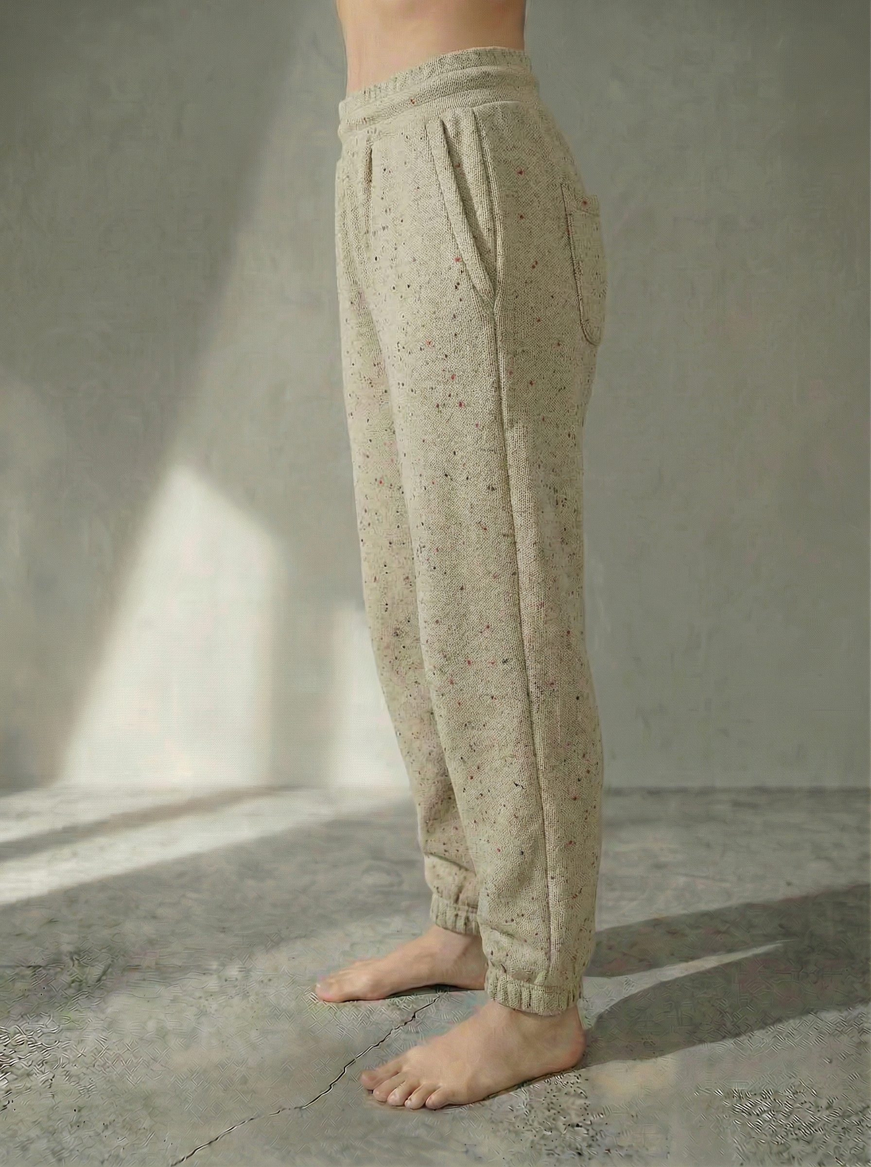 Side view of the Deryn women’s luxury jogger pants beige with red fleck colour, by BOU Clothing shown on a model standing barefoot against a stone grey  backdrop.