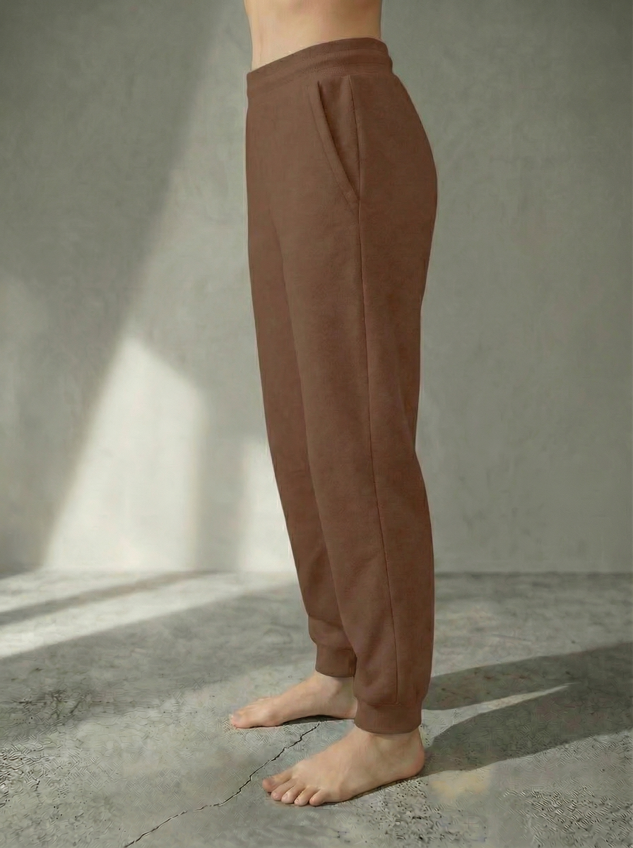 Side view of the Deryn Jogger women’s luxury jogger pants by BOU Clothing in Tan, shown on a model standing barefoot against a beige backdrop.