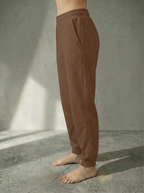 Side view of the Deryn Jogger women’s luxury jogger pants by BOU Clothing in Tan, shown on a model standing barefoot against a beige backdrop.
