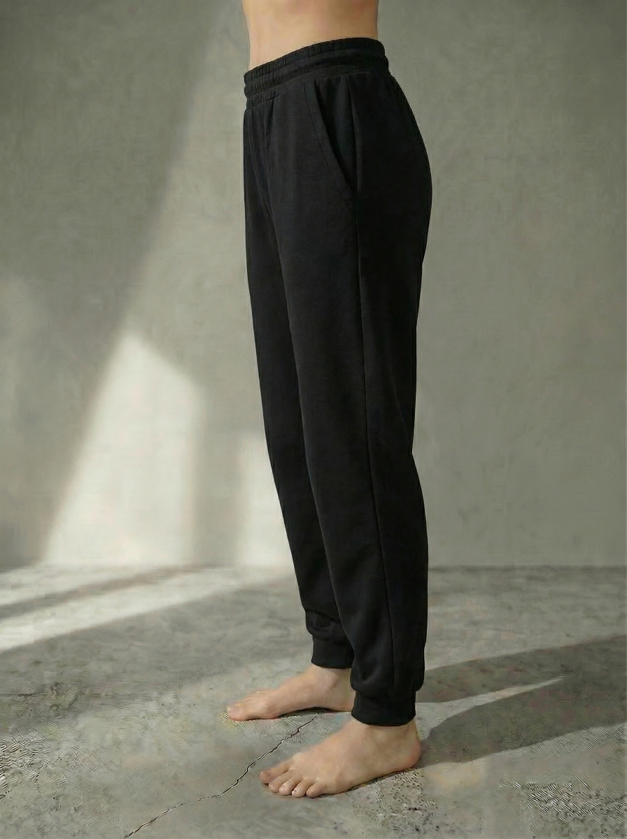 Side view of the Deryn women’s luxury jogger pants Black colour, by BOU Clothing shown on a model standing barefoot against a stone grey  backdrop.