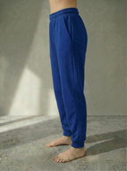 Side view of the Deryn women’s luxury jogger pants Cornflower colour, by BOU Clothing shown on a model standing barefoot against a stone grey  backdrop.