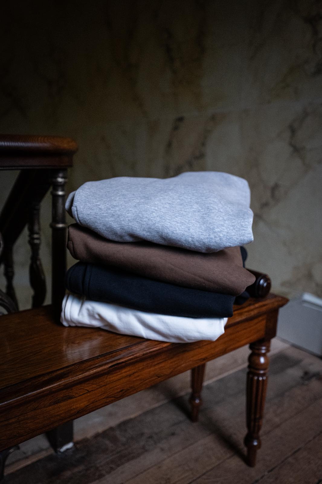 Stack of folded clothes on a wooden bench against a textured wall.