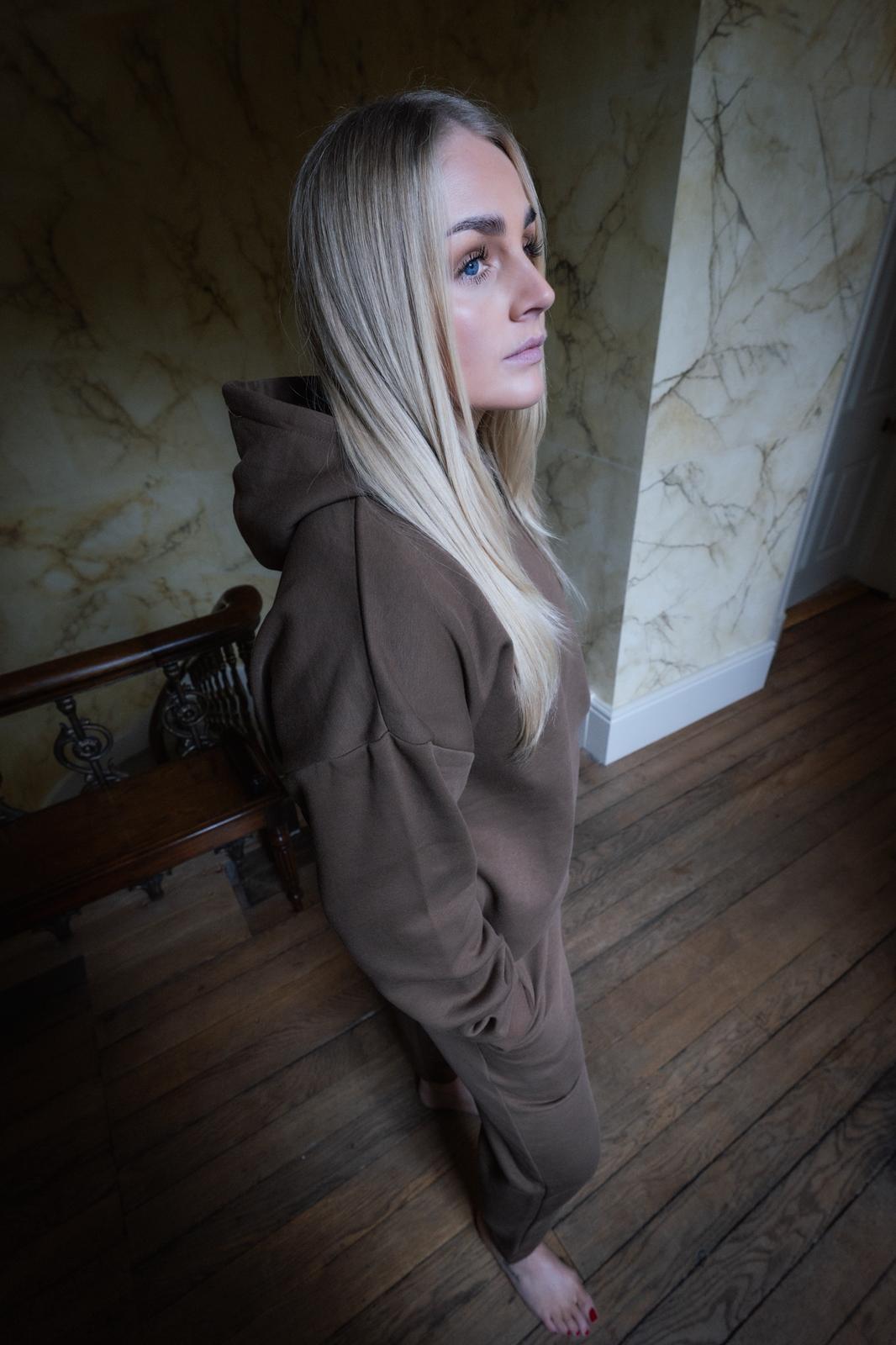 Woman in a brown hoodie standing in a room with marble walls and wooden floor.