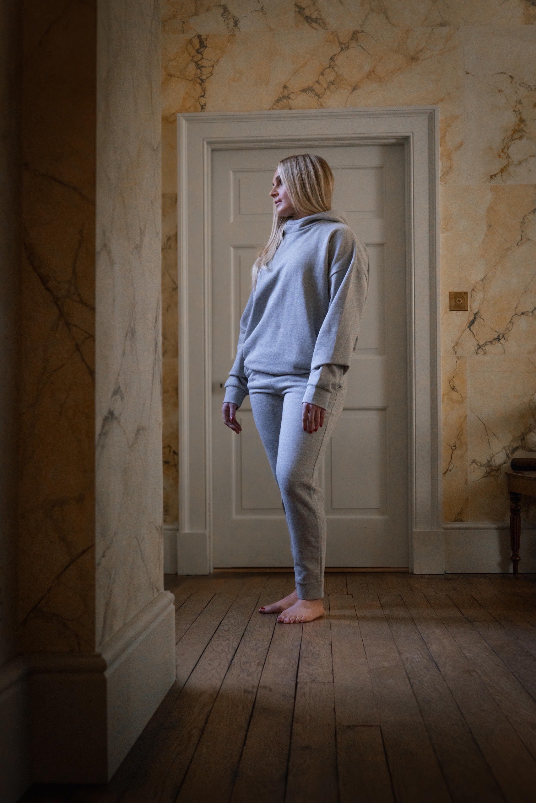 woman wearing a grey hoodie and sweat pants in a wooden corridor