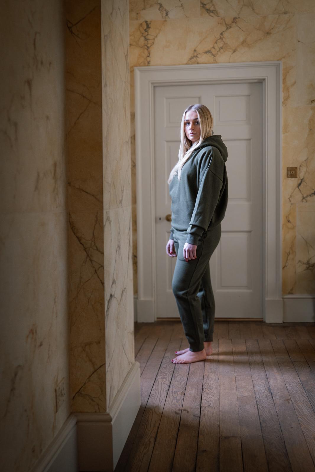 Person wearing a green tracksuit standing in a room with marble walls and wooden floor.