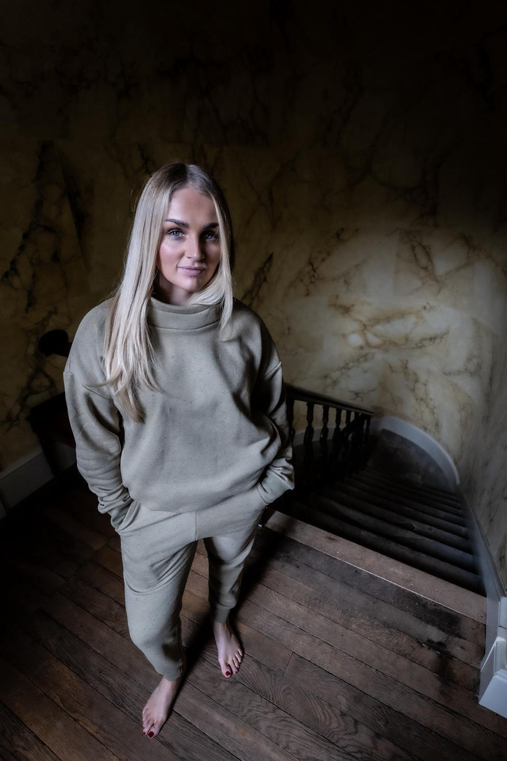 Woman in a beige outfit standing on a staircase with a marble wall in the background
