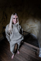 Woman in a beige outfit standing on a staircase with a marble wall in the background