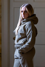 Woman wearing a gray hoodie and pants in a neutral setting