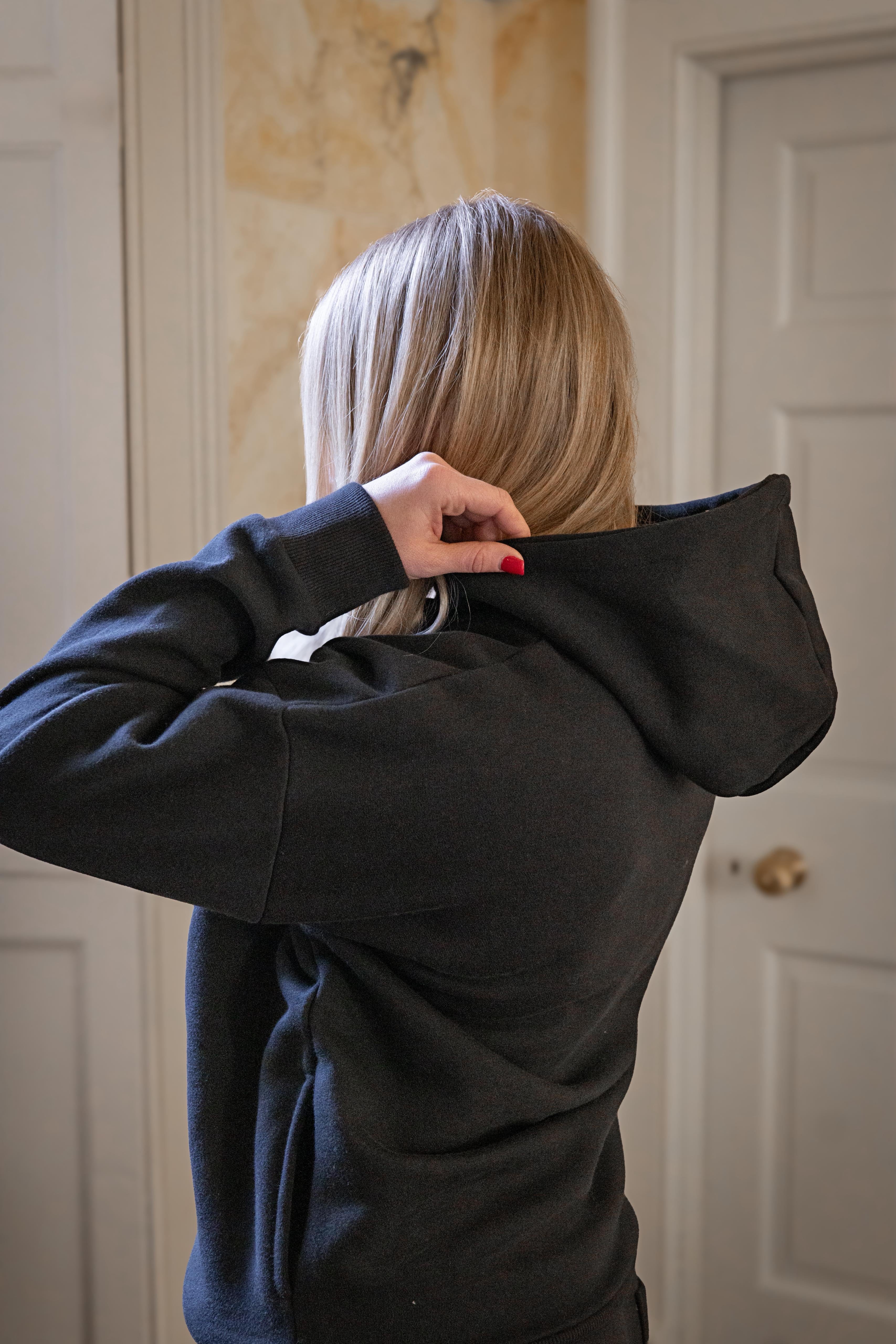 Person wearing a black hoodie with their back to the camera indoors.