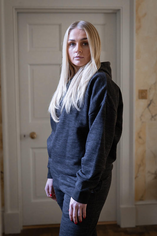 Woman wearing a dark hoodie standing in a room with a white door and marble wall.