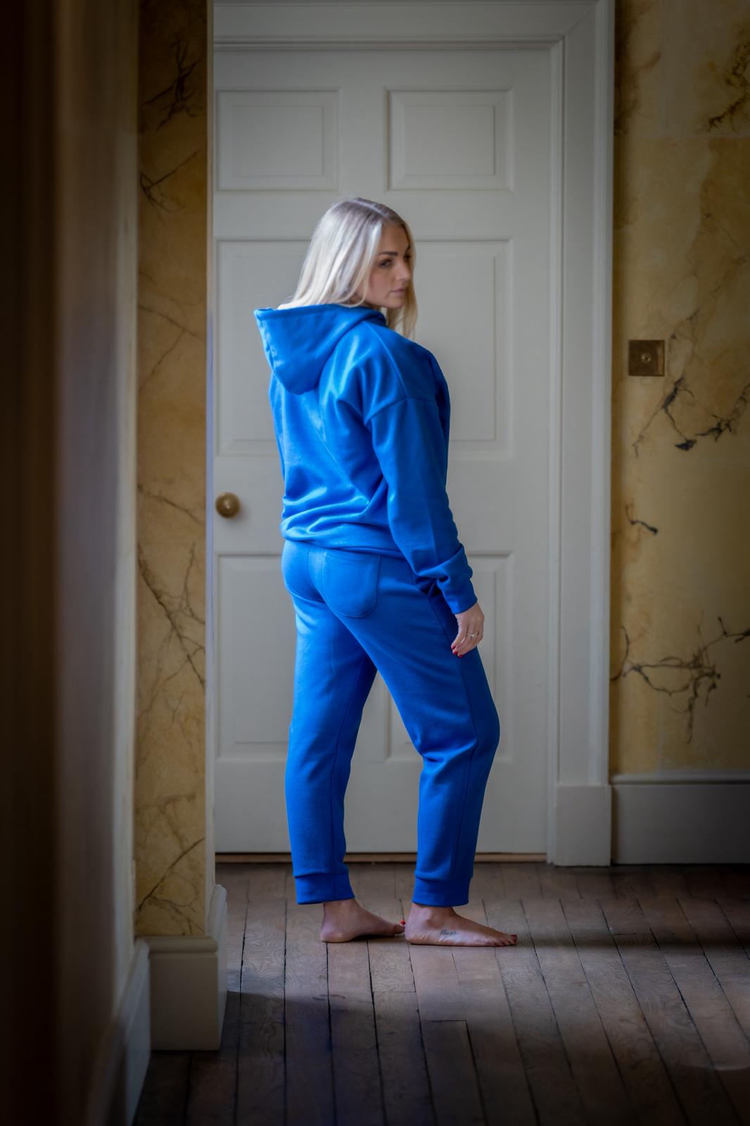 Person wearing a blue hoodiw and joggers standing in a room with a white door and marble walls.