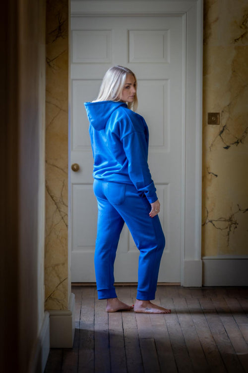 Person wearing a blue hoodiw and joggers standing in a room with a white door and marble walls.